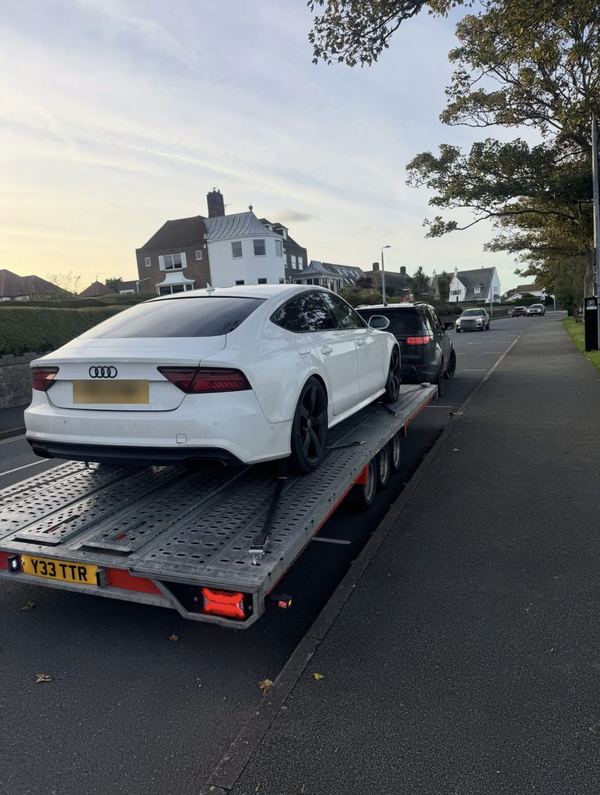 White Audi A7 strapped onto the transporter at dusk on a seaside road