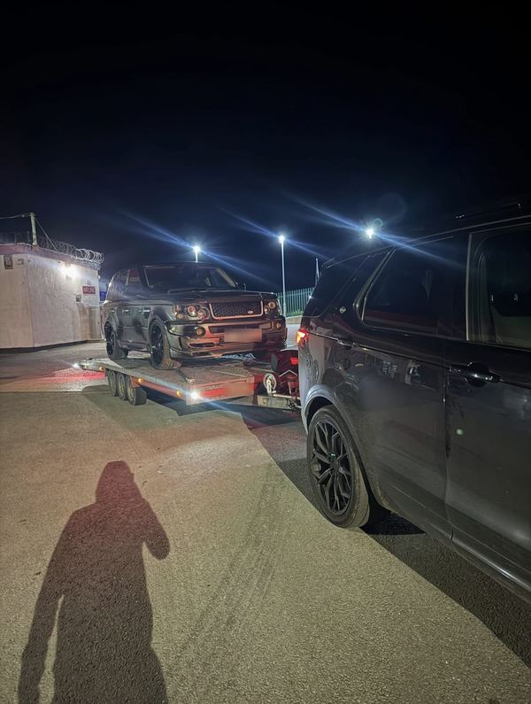 Range Rover Sport loaded on the trailer at night under floodlights, with the Discovery alongside
